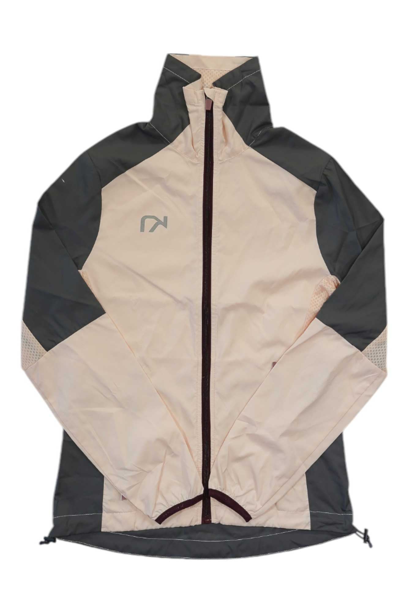 The Kari Traa Womens Nora Jacket is a lightweight shell with a full front zipper, light beige fabric, and dark gray panels on the sides, shoulders, and sleeves, plus a small geometric logo on the left chest.
