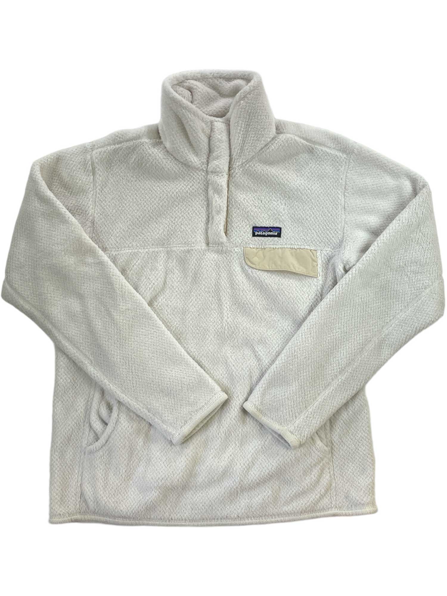 The Women's Re-Tool Snap-T Pullover is a cream long-sleeve recycled polyester fleece with Polartec Thermal Pro for warmth. It features a stand-up collar, snap placket, side pockets, and a contrasting chest pocket with the Patagonia logo.
