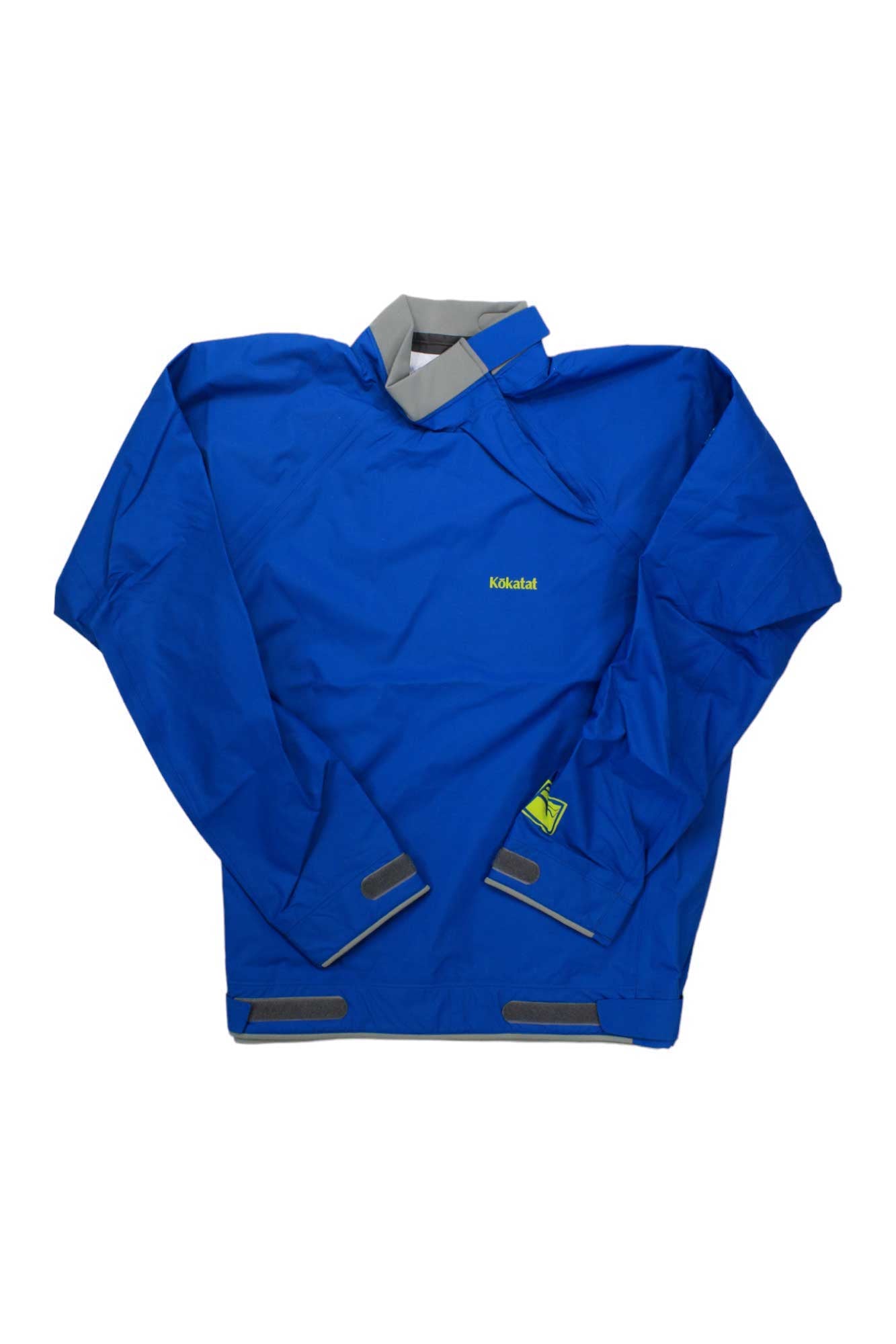 The Kokatat Men's Stance Jacket is a blue long-sleeve paddling jacket with adjustable neoprene waist, gray closures at neck, wrists, and waist, made from waterproof breathable fabric. The yellow Kokatat logo appears on the chest. Laid flat on white background.