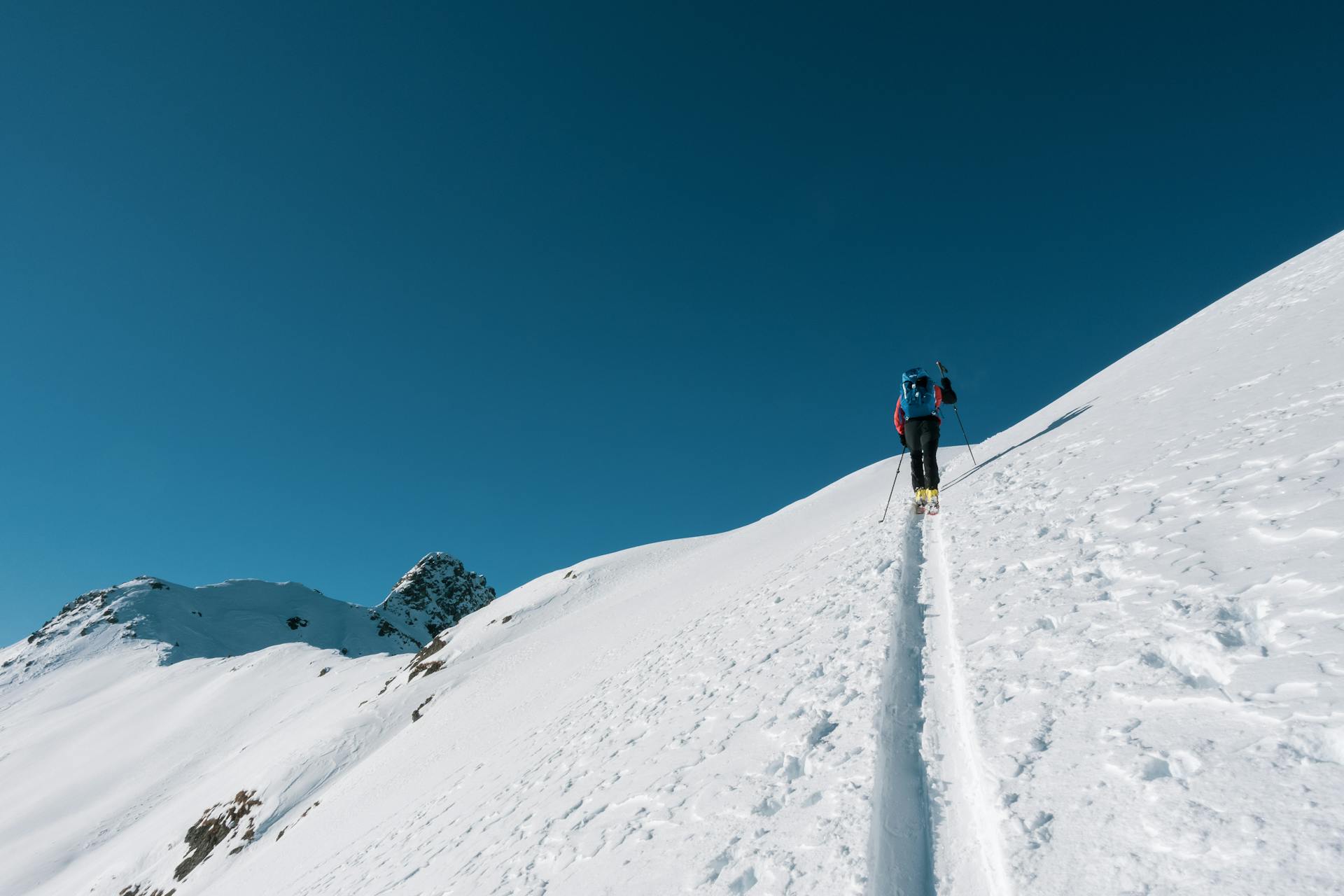 A person skiing up a snowy hill with a blue sky ahead of them.