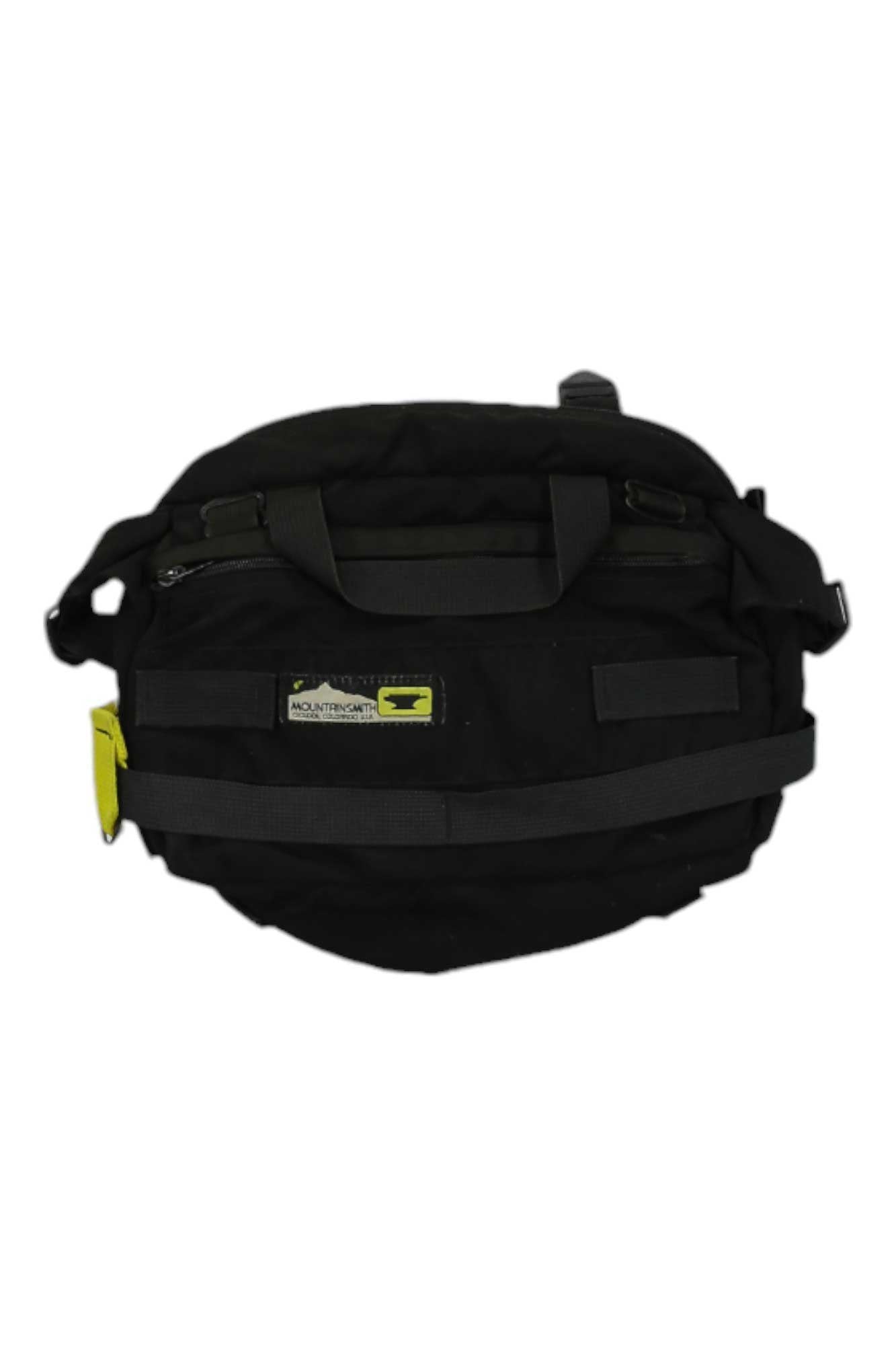 The Tour TLS Waistpack is a black bag with short handles, a shoulder strap, a yellow side tag, and a rectangular patch featuring text and a small yellow graphic—ideal for outdoor adventures.