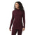 A woman with curly hair stands smiling, wearing the Smartwool Womens Thermal Merino Drape Neck Hoodie and matching pants, her hands relaxed by her sides as she faces slightly to the side.