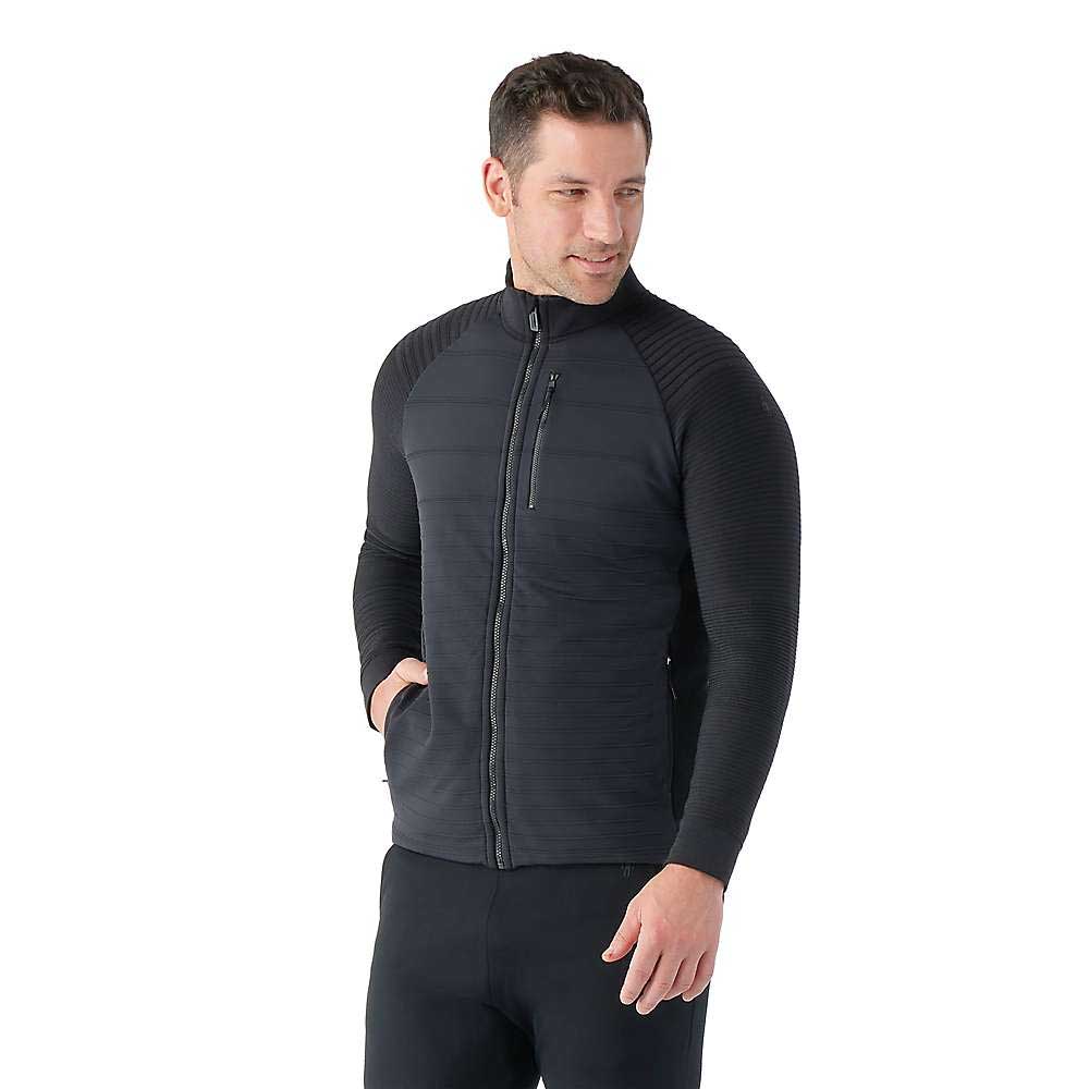 A man wears the Smartwool Men's Intraknit Merino Insulated Jacket—black, fitted, with ribbed sleeves and side pockets—standing slightly to the side, looking down with a slight smile against a plain white background.