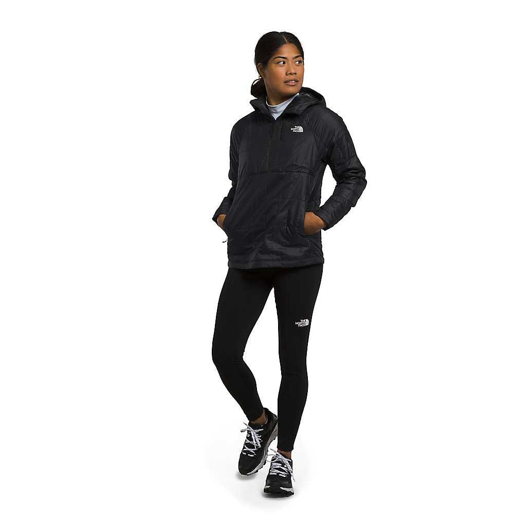 A woman in a black The North Face Womens Circaloft 1/4 Zip Pullover with synthetic insulation, black leggings, and black sneakers poses with hands in her pockets, looking sideways against a plain white background.