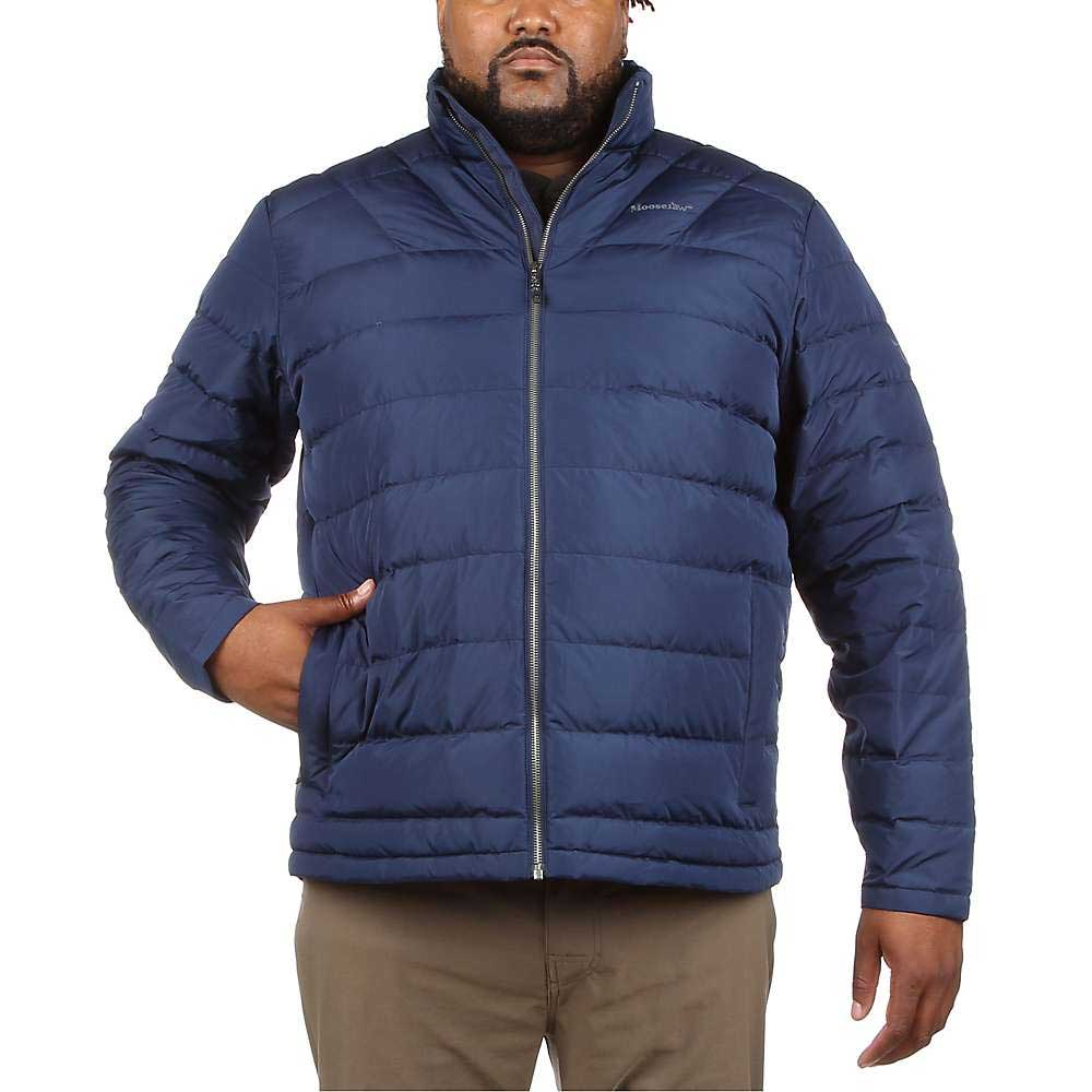A man wears the Moosejaw Mens Down Insulator Jacket in blue—a water-resistant, responsibly sourced down jacket with a zip-up front and standing collar. He has one hand in his pocket and pairs it with light brown pants.