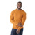 A man in a fitted, long-sleeve, orange Smartwool Mens Sparwood Crew Sweater and dark jeans stands against a white background, smiling and touching his left arm with his right hand.