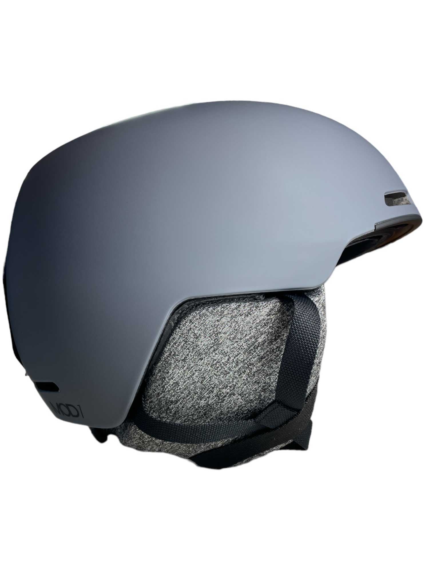 The Oakley Mod1 Helmet features a sleek matte gray finish, black and gray fabric ear covers, and a black adjustable chin strap in a modern skate-style design, shown in side profile against a white background.