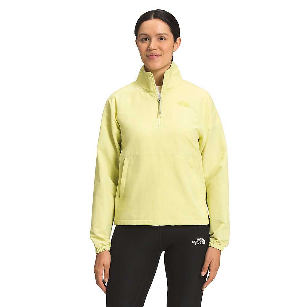 A woman faces forward wearing The North Face Womens Class V Windbreaker in light yellow, made from recycled materials with a high collar, and black leggings. The North Face logos appear on the chest and leg. Background is white.