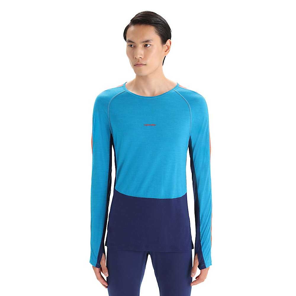 A man faces forward wearing the Icebreaker Men's 125 ZoneKnit LS Crewe, a long-sleeve, two-tone athletic shirt in light blue and navy Cool-Lite fabric, with navy pants against a plain white background.