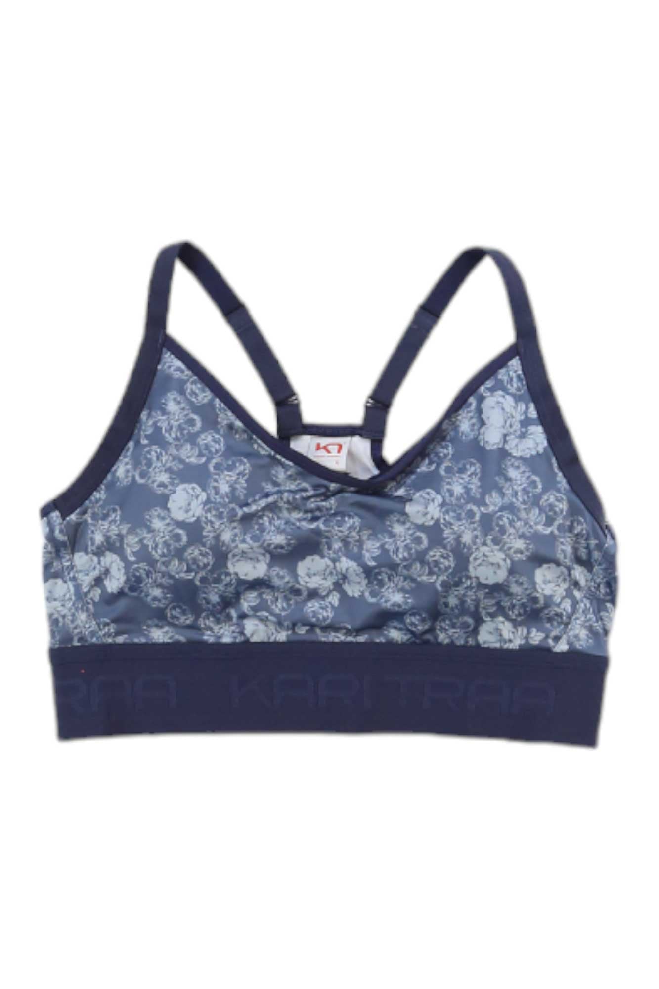 The Kari Traa Women's Froya Bra is a blue sports bra with a floral pattern, adjustable shoulder straps, and a wide elastic band at the bottom featuring the Kari Traa brand name.