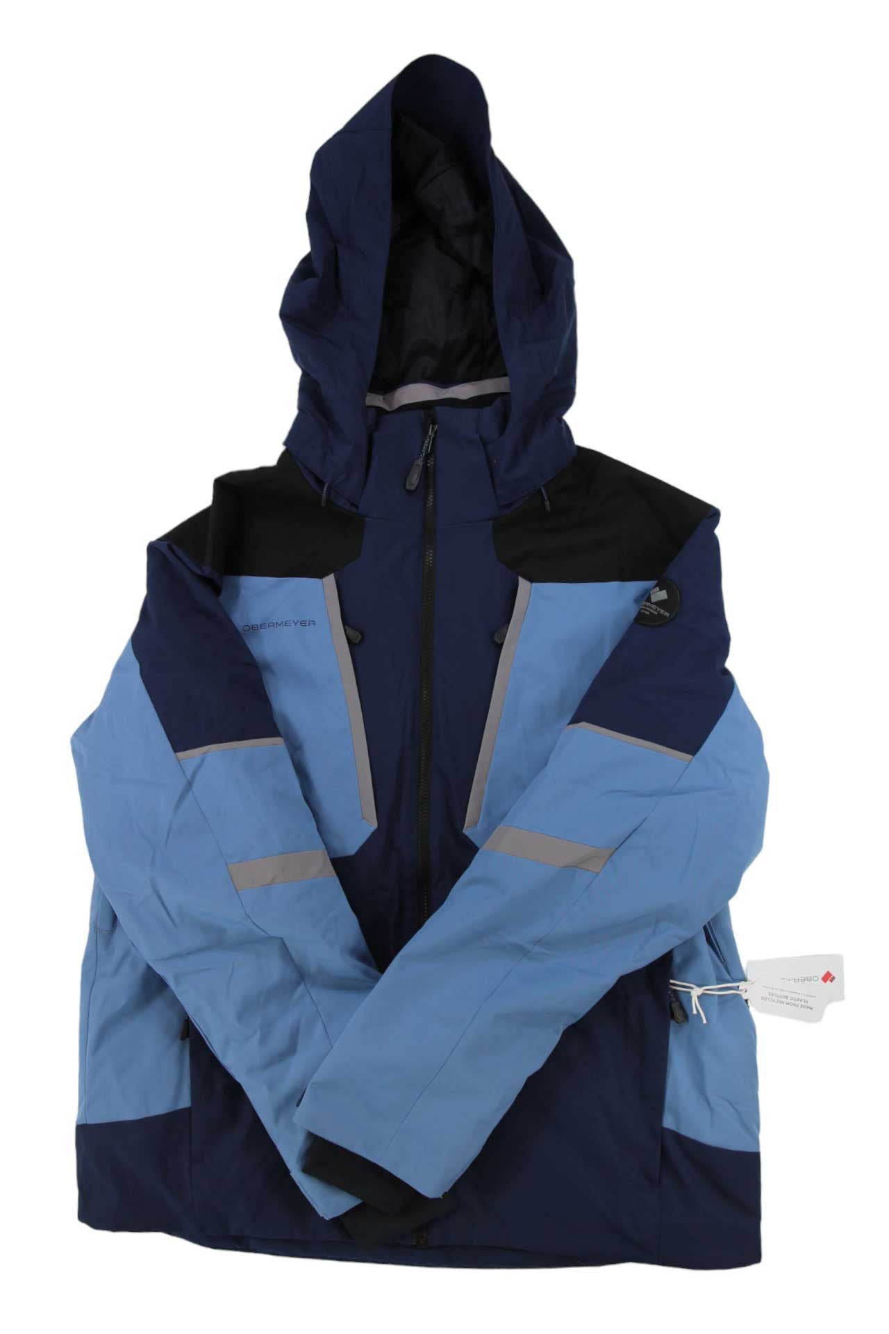 The Obermeyer Men's Foundation Jacket is a blue and navy ski jacket with black shoulder panels, front zipper, two zip pockets, reflective strip accents, a right sleeve tag, recycled material construction, and HydroBlock Pro weather protection.