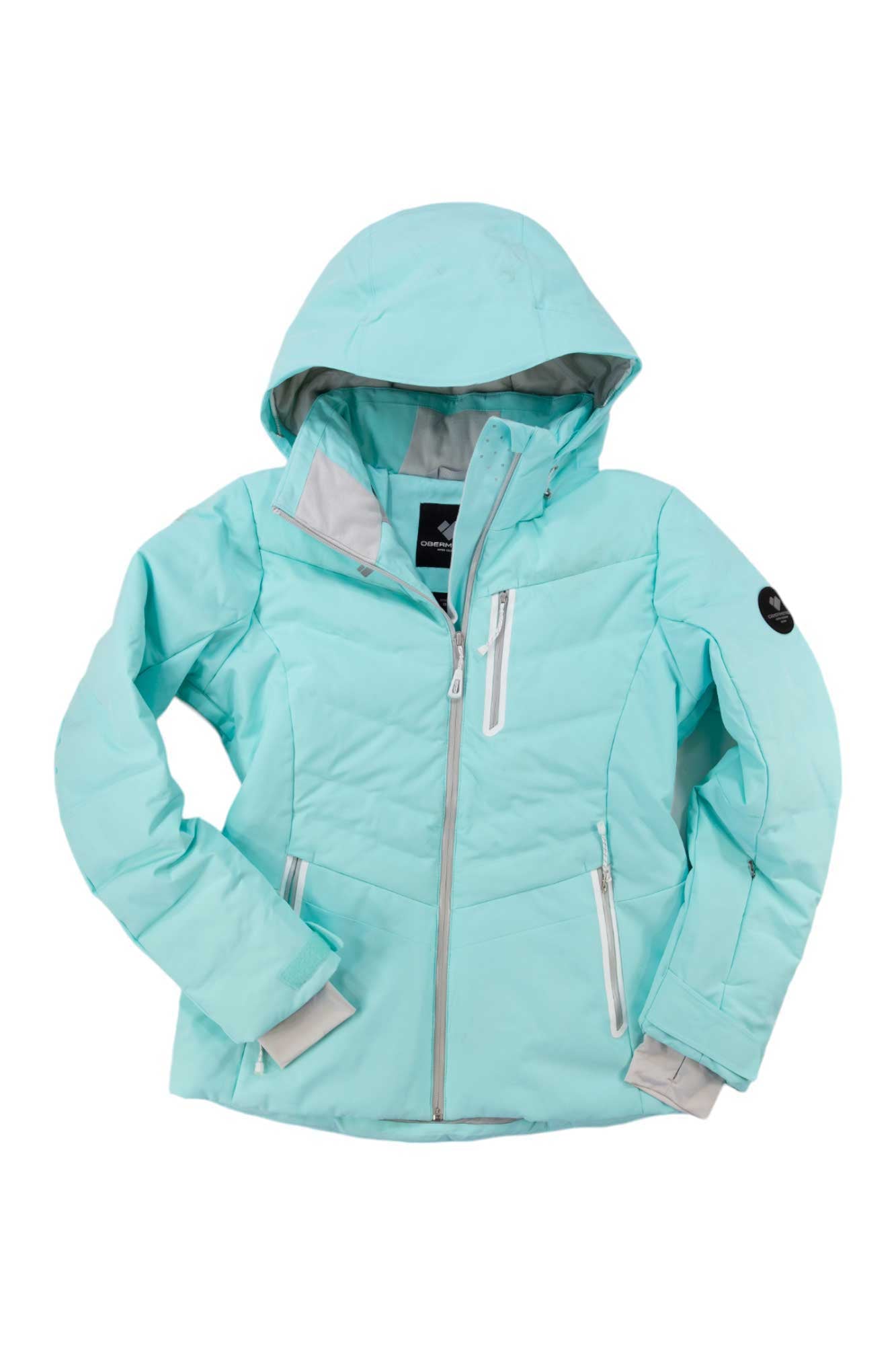 The Obermeyer Womens Cosima Down Jacket is a light blue insulated winter jacket featuring gray zipper accents and three zippered pockets, shown on a white background.