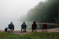 people sitting in camp chairs by a lake