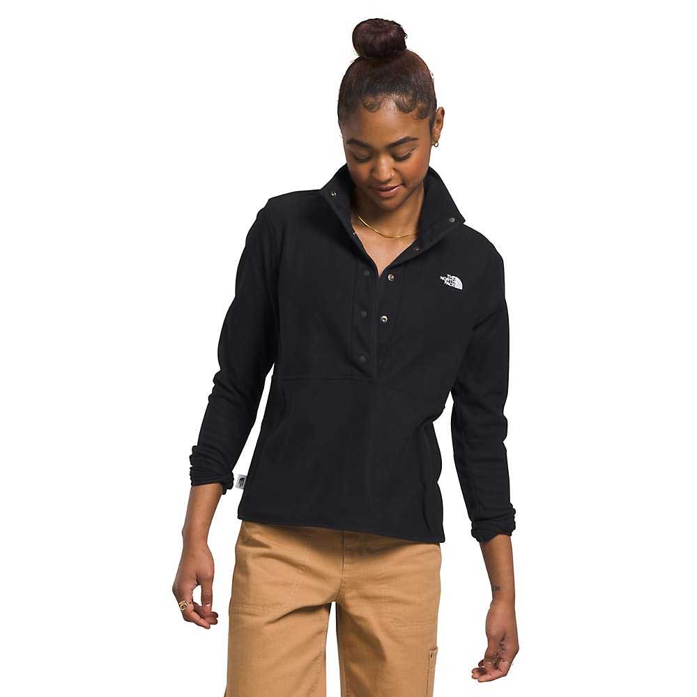 A woman wears The North Face Womens Alpine Polartec 100 1/2 Snap Top in black with tan pants, standing with her head slightly down and looking to the side, one hand relaxed by her side and the other near her pocket.