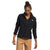 A woman wears The North Face Womens Alpine Polartec 100 1/2 Snap Top in black with tan pants, standing with her head slightly down and looking to the side, one hand relaxed by her side and the other near her pocket.