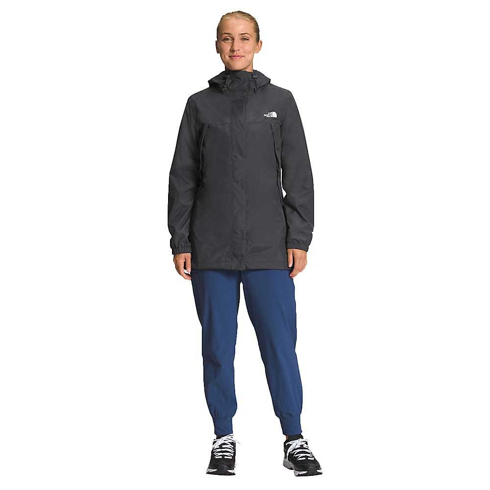 A woman faces forward against a plain white background, wearing The North Face Womens Antora Parka in black, paired with blue jogger pants and black sneakers with white soles.