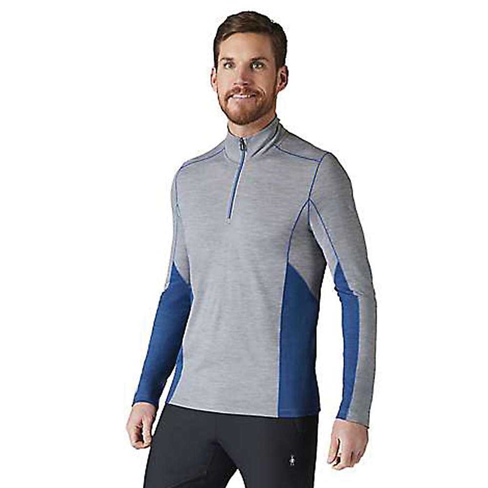 A bearded man is wearing the Smartwool Men's Merino Sport 150 LS 1/4 Zip Top in gray and blue with black pants, standing and smiling against a plain white background.