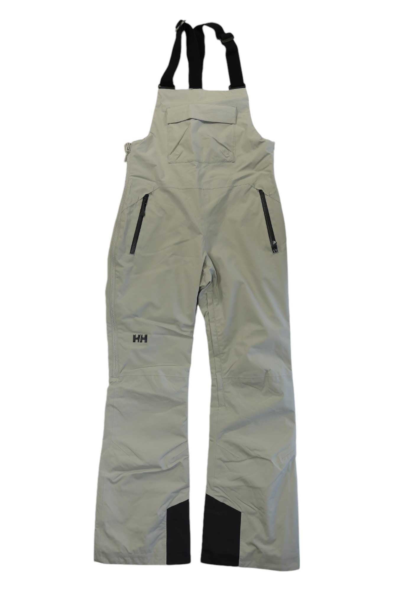 The Helly Hansen Womens Legendary Insulated Bib Pant in light gray features black adjustable straps, zippered side pockets, reinforced lower leg patches, and the HH logo on the left thigh. Stay warm and dry all day in these insulated snow pants.