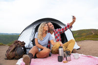 a man and woman sitting on a picnic blanket while taking a selfie