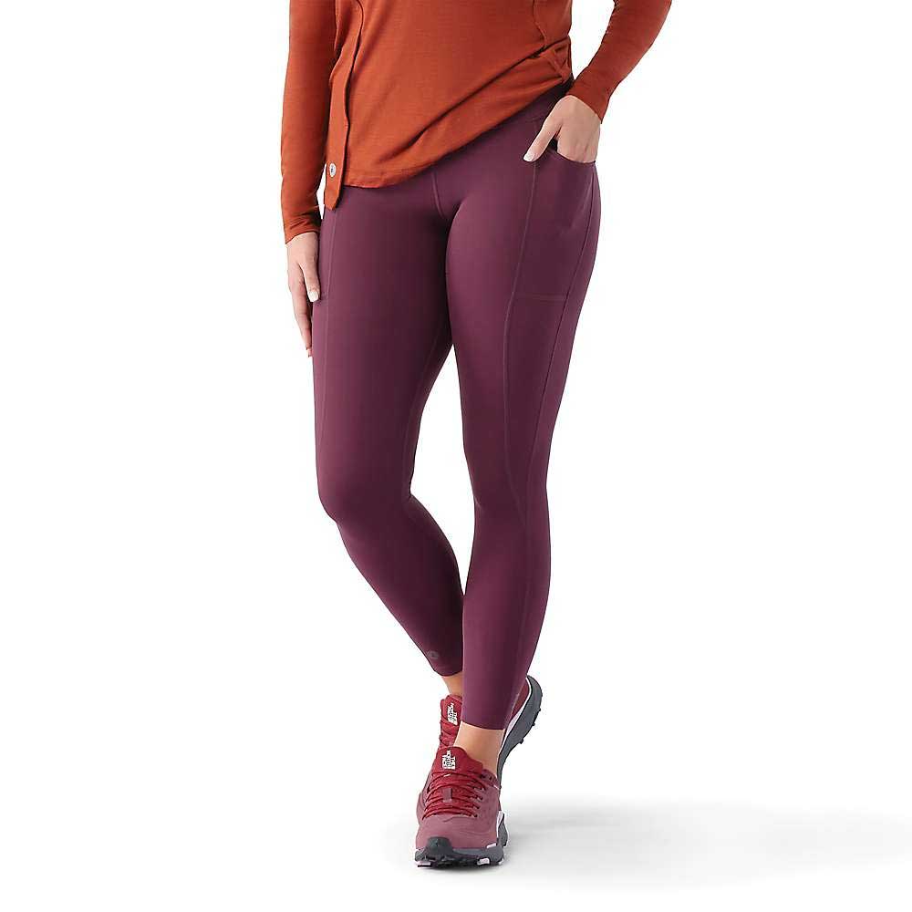 A person stands with one hand in their pocket, wearing a long-sleeve orange top and burgundy Smartwool Womens Active Legging with matching sneakers against a white background. Their head is not visible.