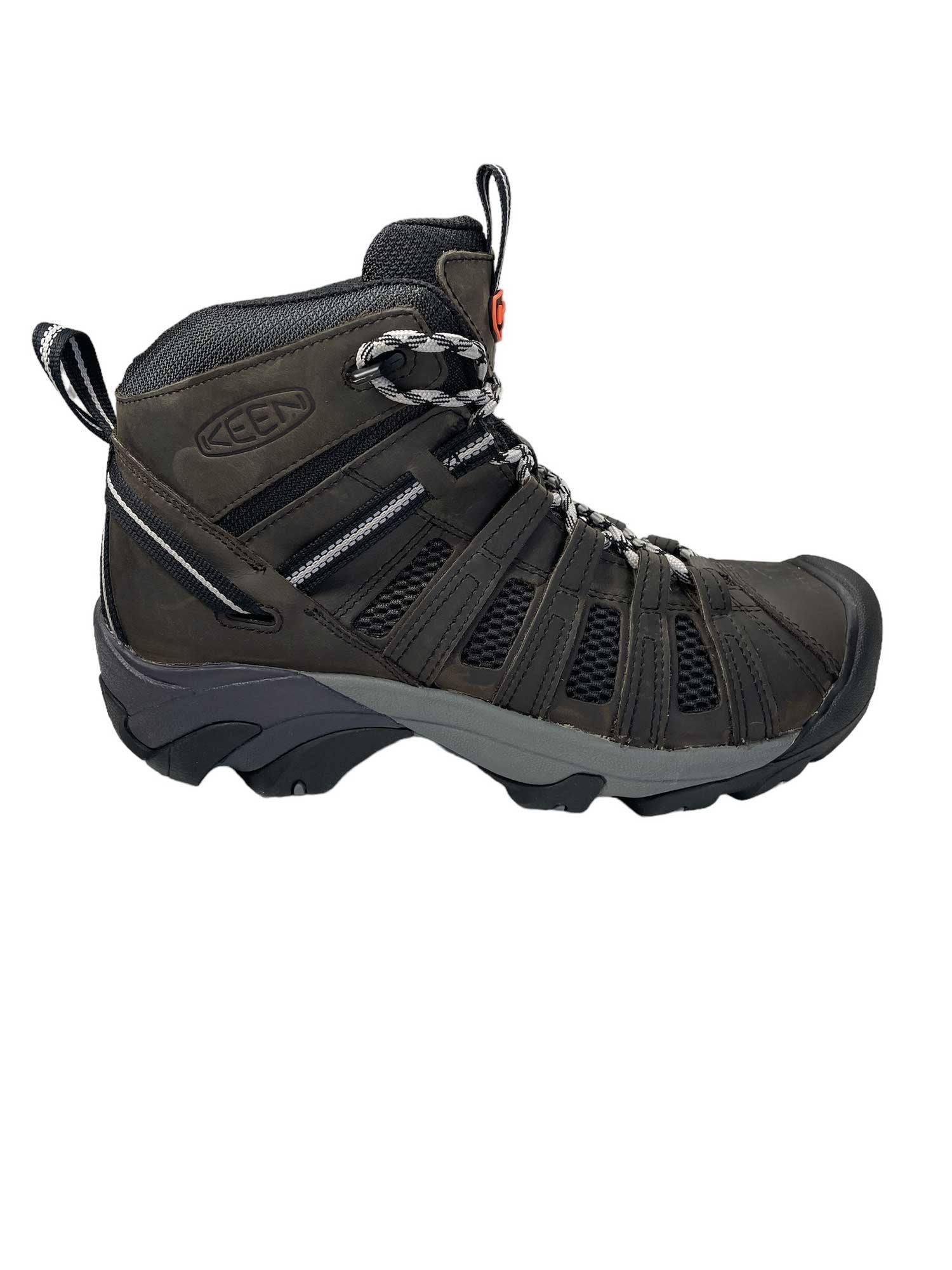 The KEEN Women's Voyageur Mid Boot is shown in a side view on a white background, featuring a dark gray and black design with breathable mesh upper, secure laces, rugged rubber sole, and heel pull loop.