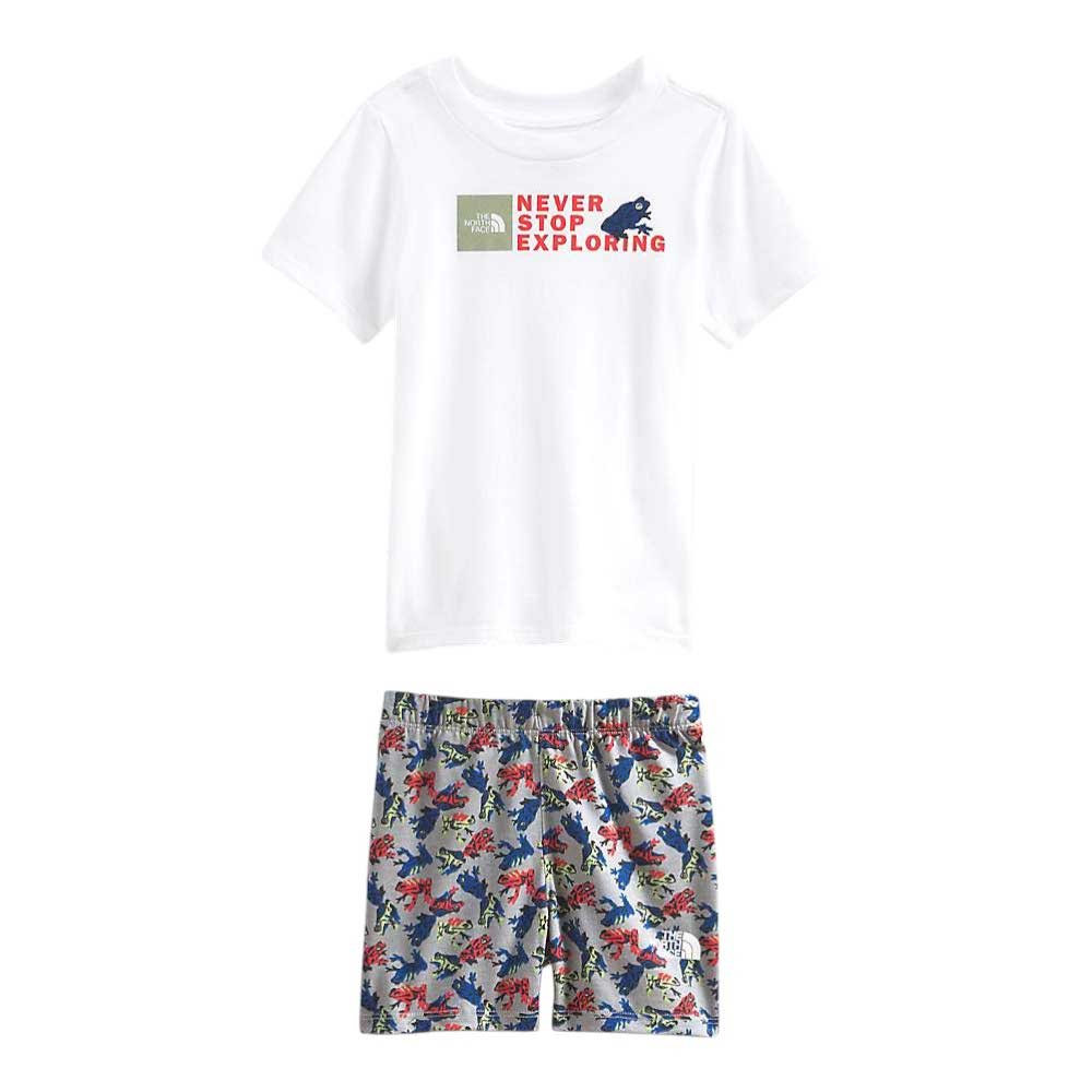 The North Face Toddlers Cotton Summer Set features a white short-sleeve tee with "Never Stop Exploring" and graphic on the chest, paired with blue shorts with a red and blue dinosaur print—perfect for playful summer days.