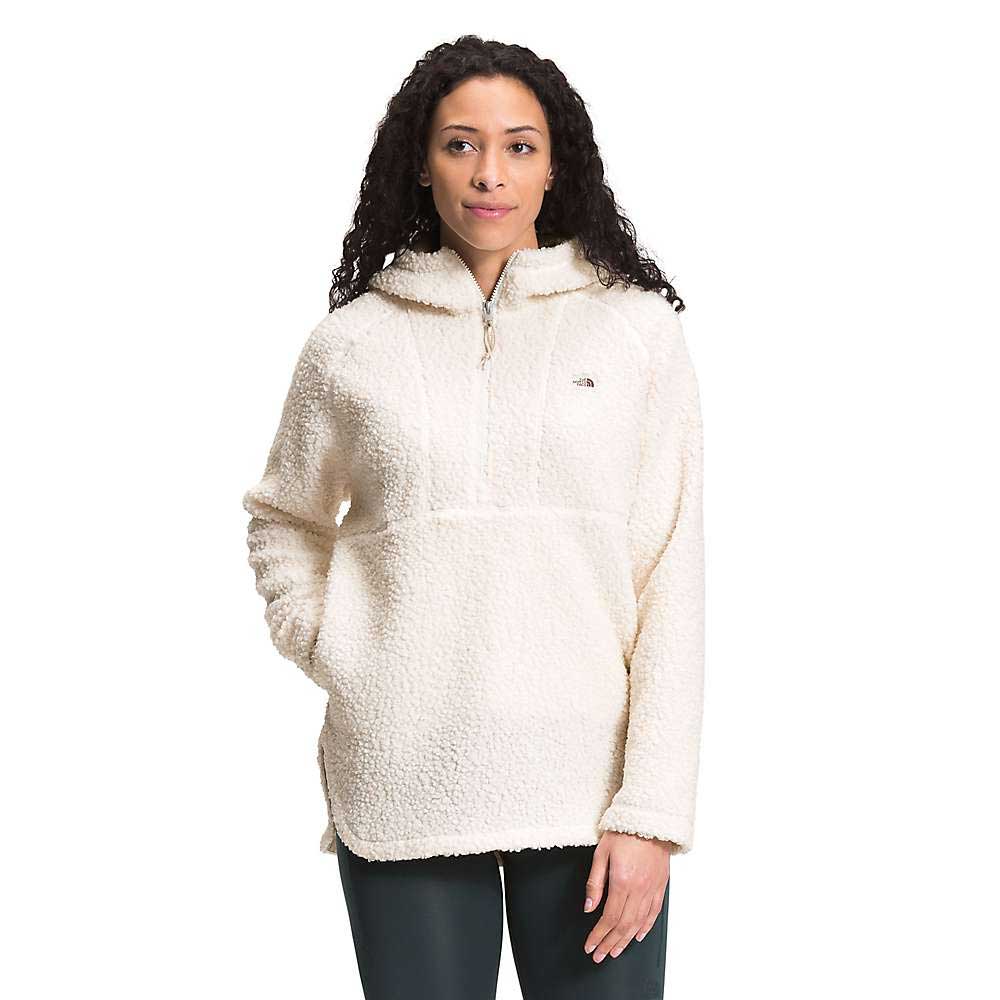 A woman with long curly hair wears the Womens Ridge Fleece Tunic, a cream-colored sherpa pullover with a quarter zip and front pocket, standing against a plain white background.
