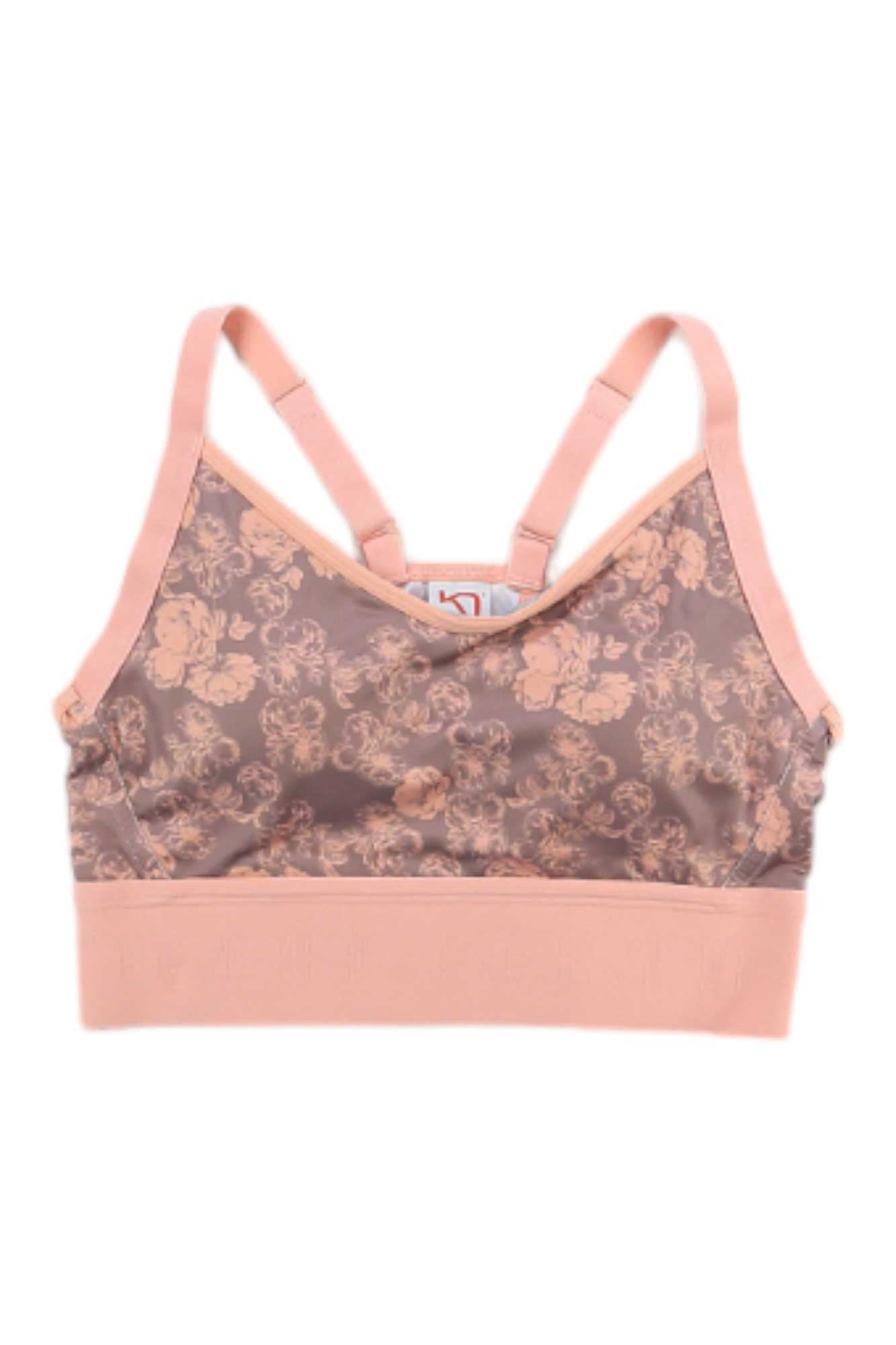 The Kari Traa Women's Froya Bra is a peach-colored bralette with adjustable straps and a floral lace front, providing light support and all-day comfort, similar to a women's sports bra.