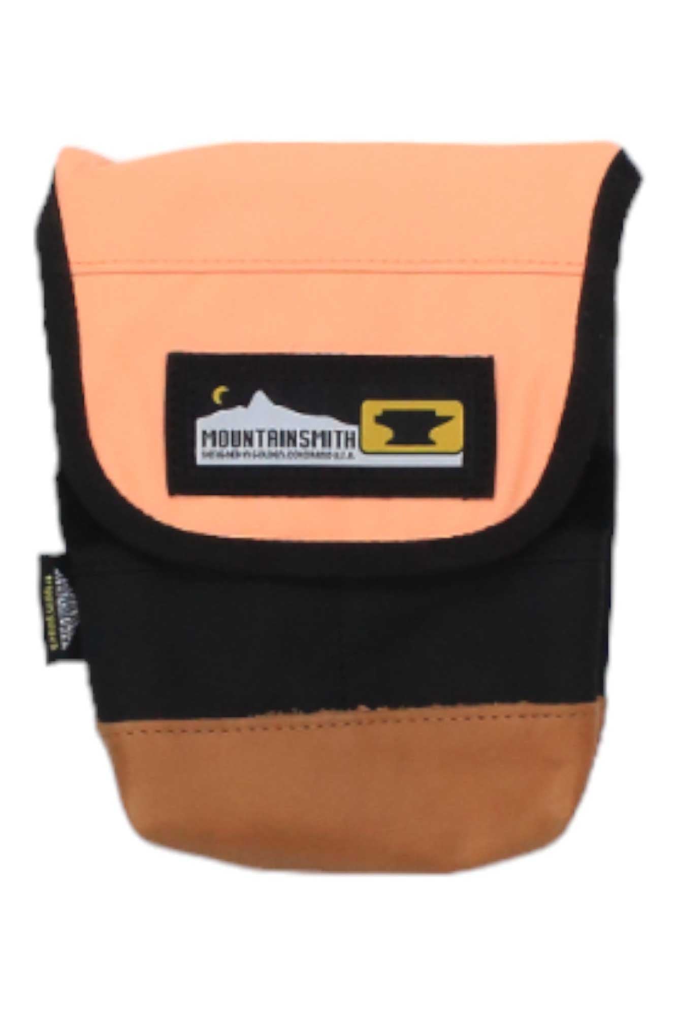 The Mountainsmith Trippin Pouch Waistpack is a small crossbody pouch with a flap, featuring an orange top, black middle, and brown bottom. The flap showcases the Mountainsmith Trippin logo patch with a mountain graphic and anvil icon.