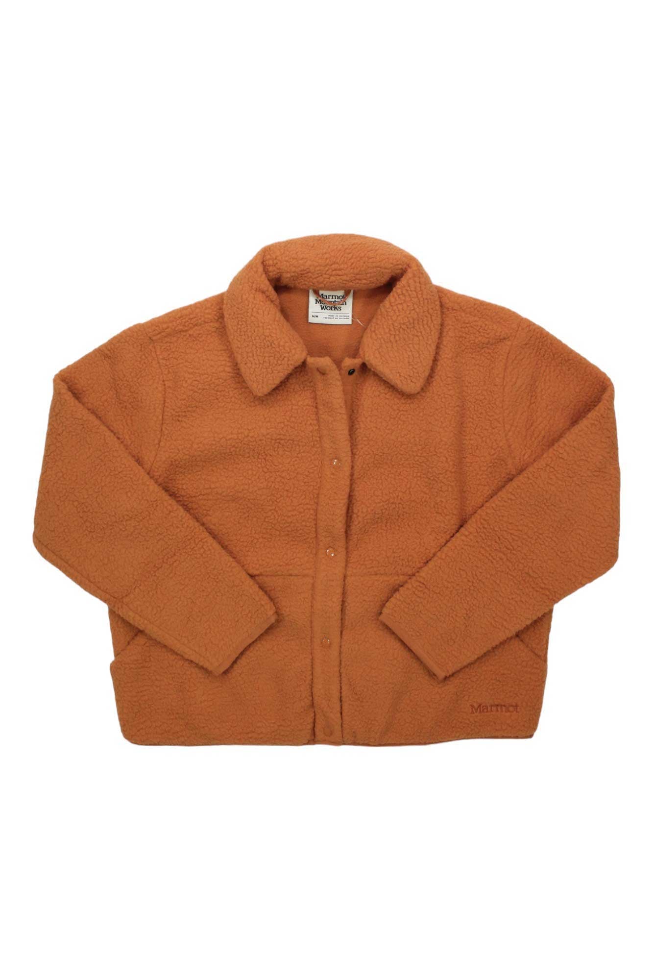 The Marmot Womens Aros Fleece Snap Jacket in burnt orange features long sleeves, a collar, snap button front, and two slit pockets. The sherpa fleece jacket is displayed flat against a white background.
