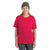 Smiling older woman with long gray hair wears a green knit beanie, dark pants, and an Icebreaker Womens Granary SS Tee in bright red, standing against a plain white background.