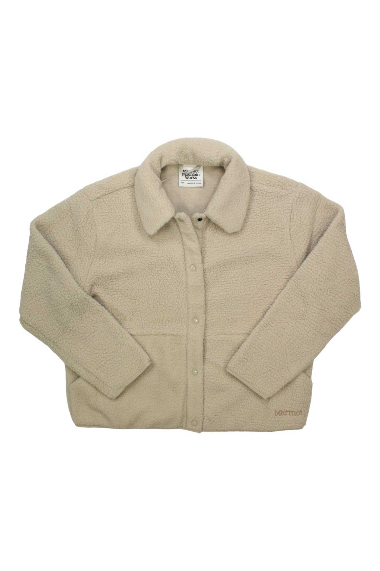 The Marmot Womens Aros Fleece Snap Jacket is a beige sherpa fleece shirt-jacket with long sleeves, a collar, and front snap buttons. It features the Marmot logo embroidered near the bottom hem, shown flat on a white background.