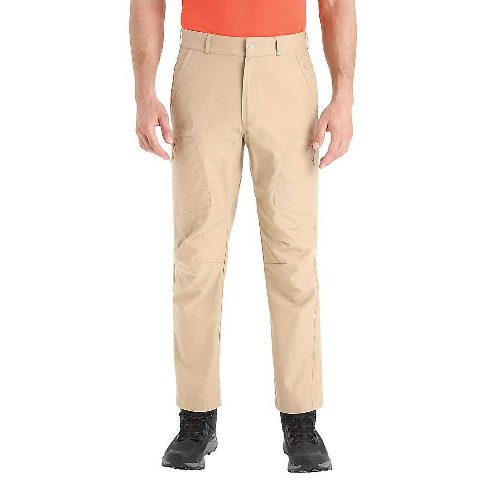 A person wearing Icebreaker Mens Hike Pant in tan, a bright orange shirt, and black shoes stands with arms relaxed at their sides against a plain white background.