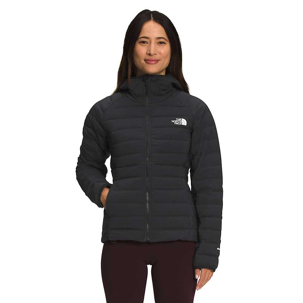 A woman wearing The North Face Womens Belleview Stretch Down Hoodie in black stands with her hands in her pockets, smiling at the camera against a plain white background.