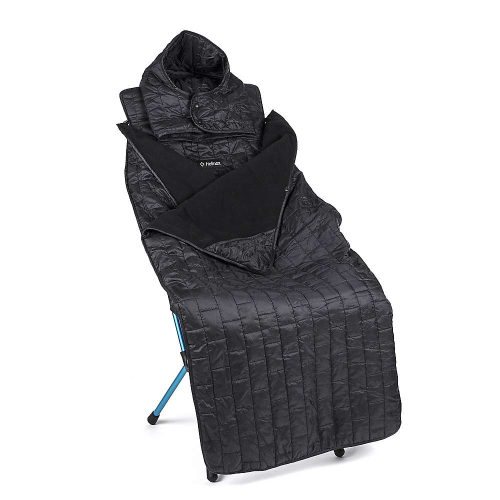 A Helinox Toasty Blanket for Sunset/Beach, a black insulated hooded camping blanket with quilted stitching and arm openings, is draped over a blue folding chair to keep you warm and comfortable outdoors.