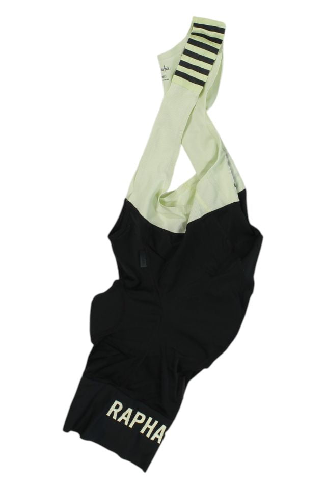 Black and light yellow Rapha Mens Pro Team Bib Shorts II - Regular with RAPHA in white on one leg, black stripes on a yellow shoulder strap, and a race-grade chamois, laid flat on a white background.