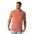 A man wearing the Smartwool Men's Active Ultralite Tech Tee in salmon with light gray shoulder and side panels, looking to his left and holding the hem of his moisture-wicking shirt.