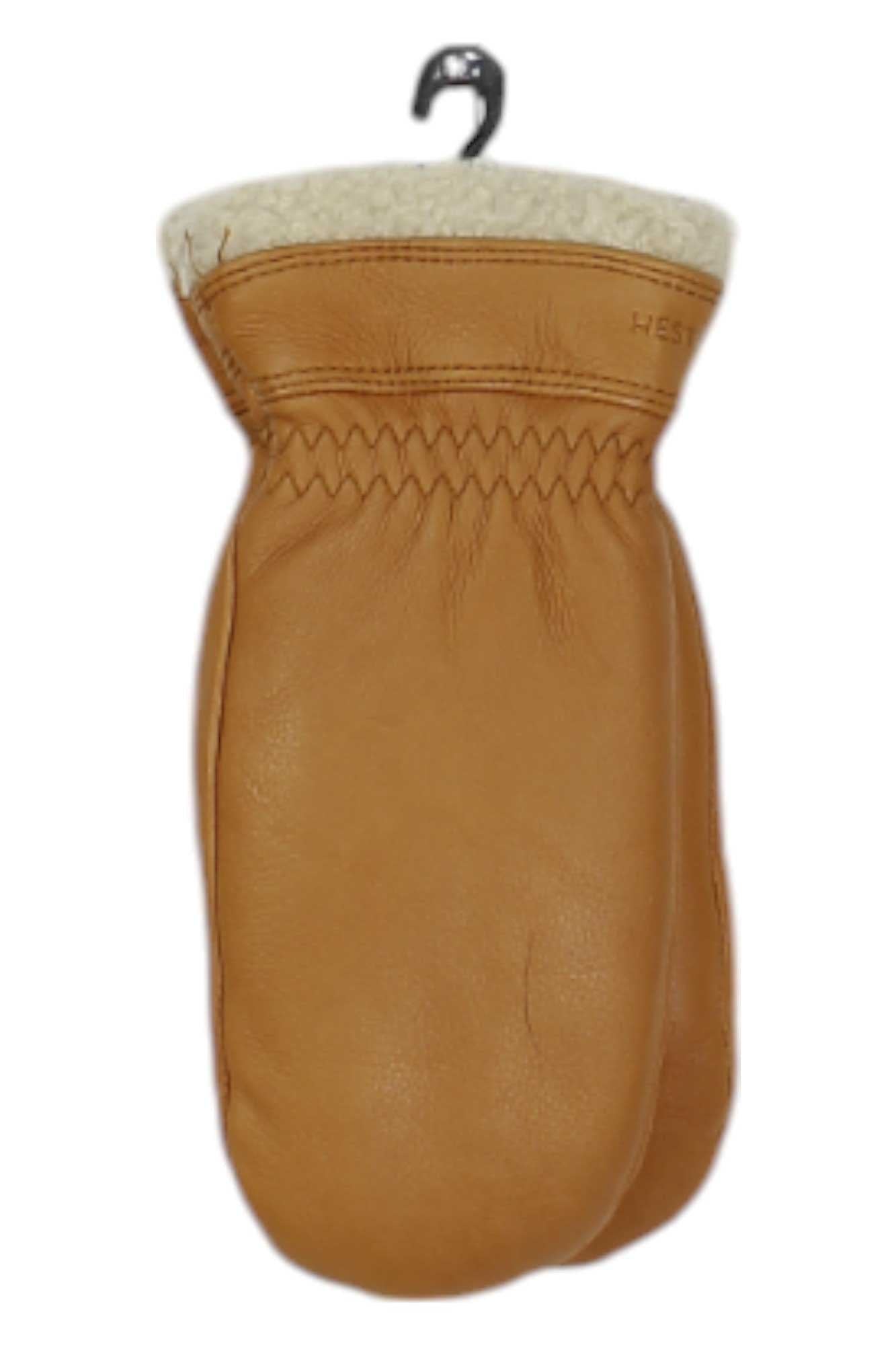 A single tan Hestra Sundborn Mitt with white fleece lining hangs from a metal hook against a white background, offering warmth and comfort for all your outdoor adventures.