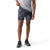 A person in a gray t-shirt and Smartwool Mens Active Lined 5 Inch Short stands against a white background, adjusting the shorts’ waistband with one hand. They wear black sneakers, and their face is not shown.
