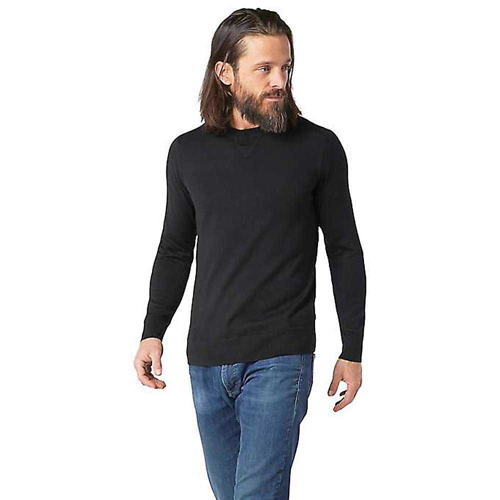 Man with long hair and a beard wears a black Smartwool Mens Sparwood Crew Sweater and blue jeans, standing and looking to his left against a plain white background.