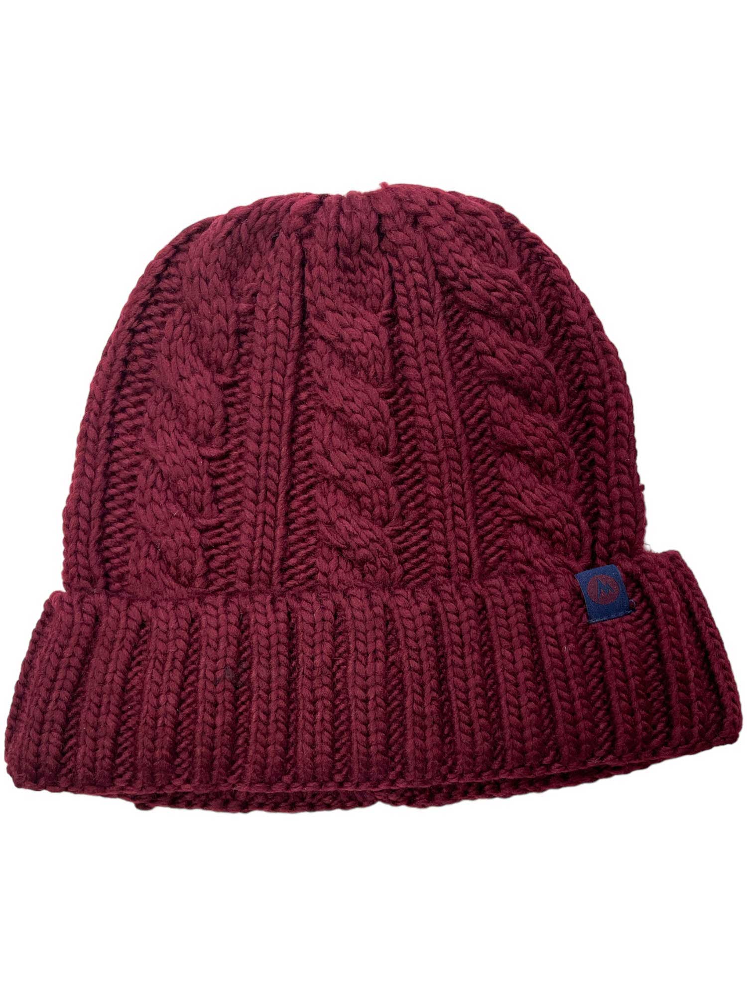 The Marmot Women's Millberry Hat is a maroon chunky knit hat with a thick ribbed fold-over cuff, cable knit pattern, and a small blue tag. It's made from recycled polyester for eco-friendly style.
