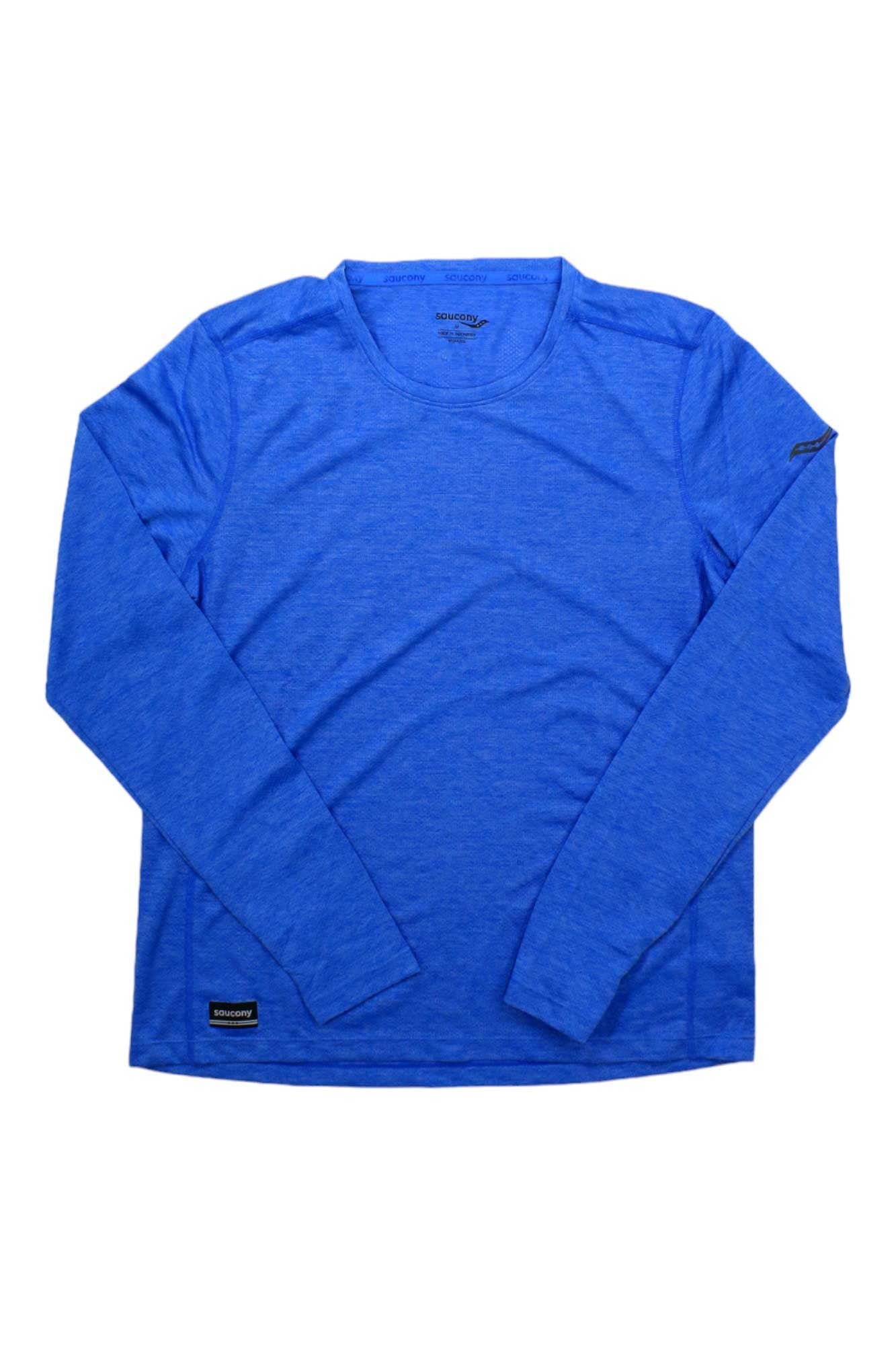The Saucony Women's Stopwatch LS Top in bright blue is laid flat on a white background, crafted from recycled polyester, and features a small black label on the lower front plus a subtle logo patch on the left sleeve.