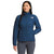 A woman with straight, dark hair smiles gently while facing forward, wearing gray pants and The North Face Womens Belleview Stretch Down Jacket in blue, featuring quilting and a front zipper. One hand is in her pocket.
