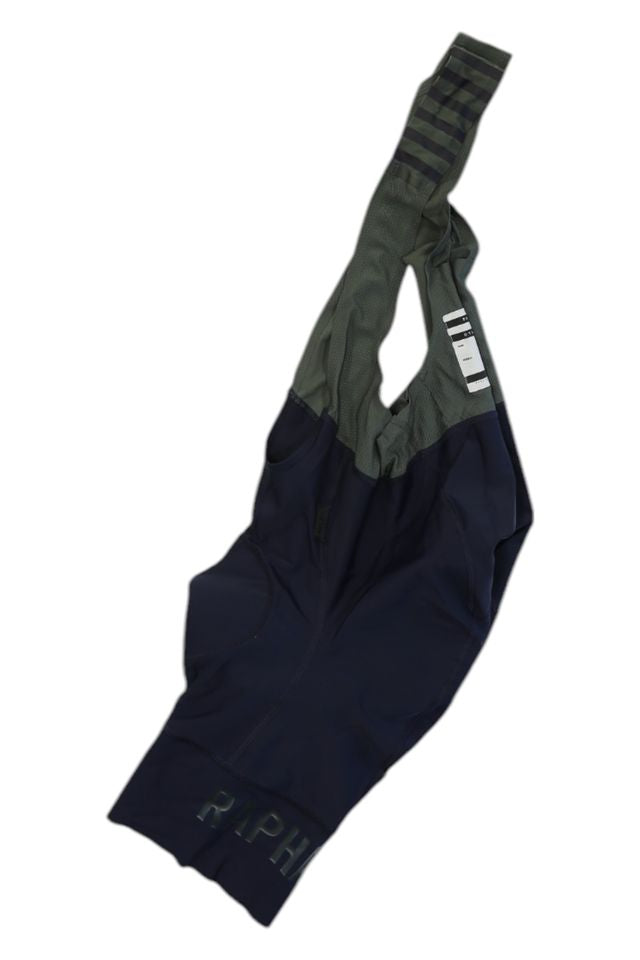A pair of Rapha Mens Pro Team Bib Shorts II - Regular, with a race-grade chamois and a two-tone design in dark navy and olive green mesh straps, is laid flat on a white background.