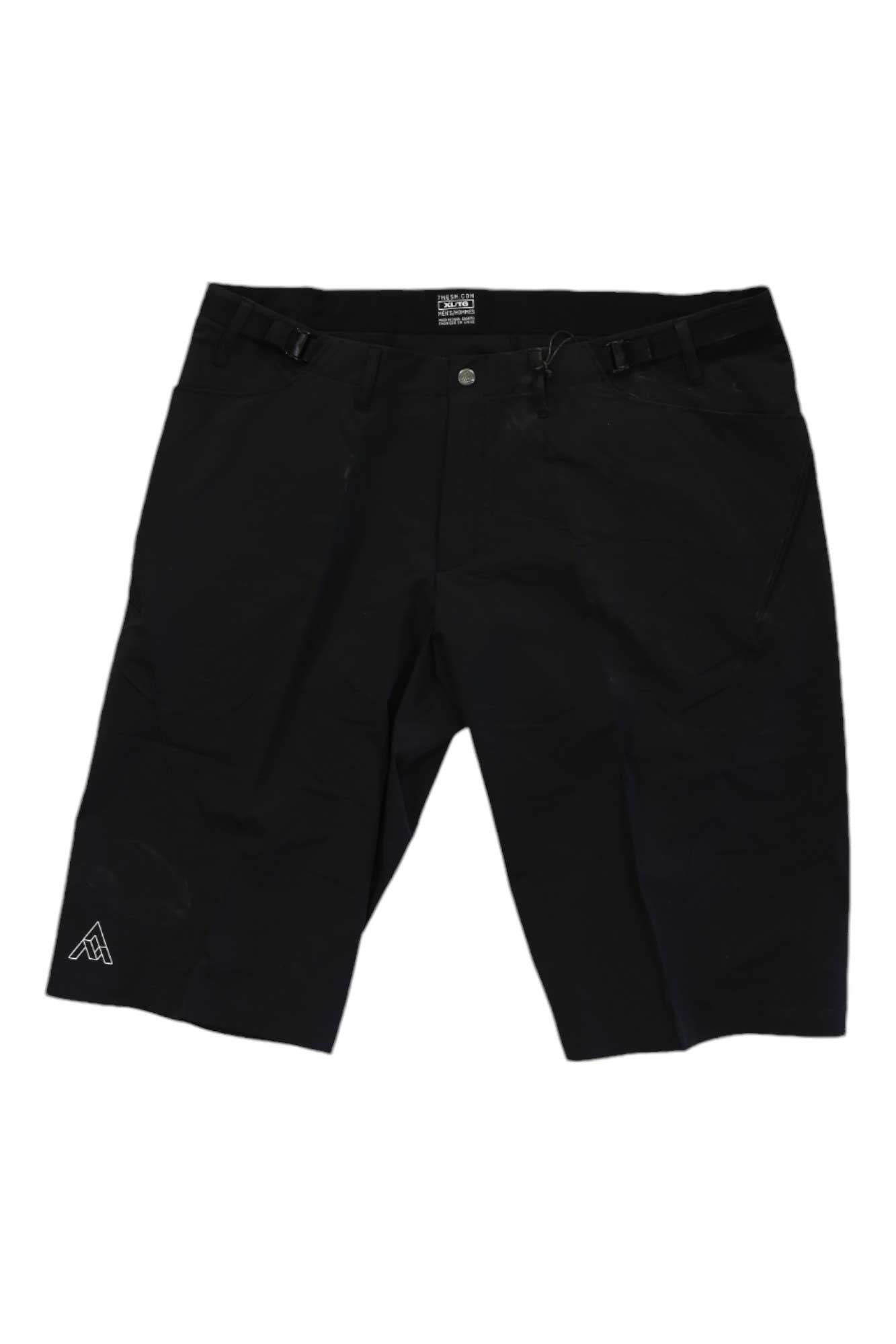 The 7mesh Mens Farside Long Short is a pair of black, knee-length cycling shorts with side pockets, belt loops, front button closure, adjustable waist for comfort, and a small white geometric logo near the left hem.