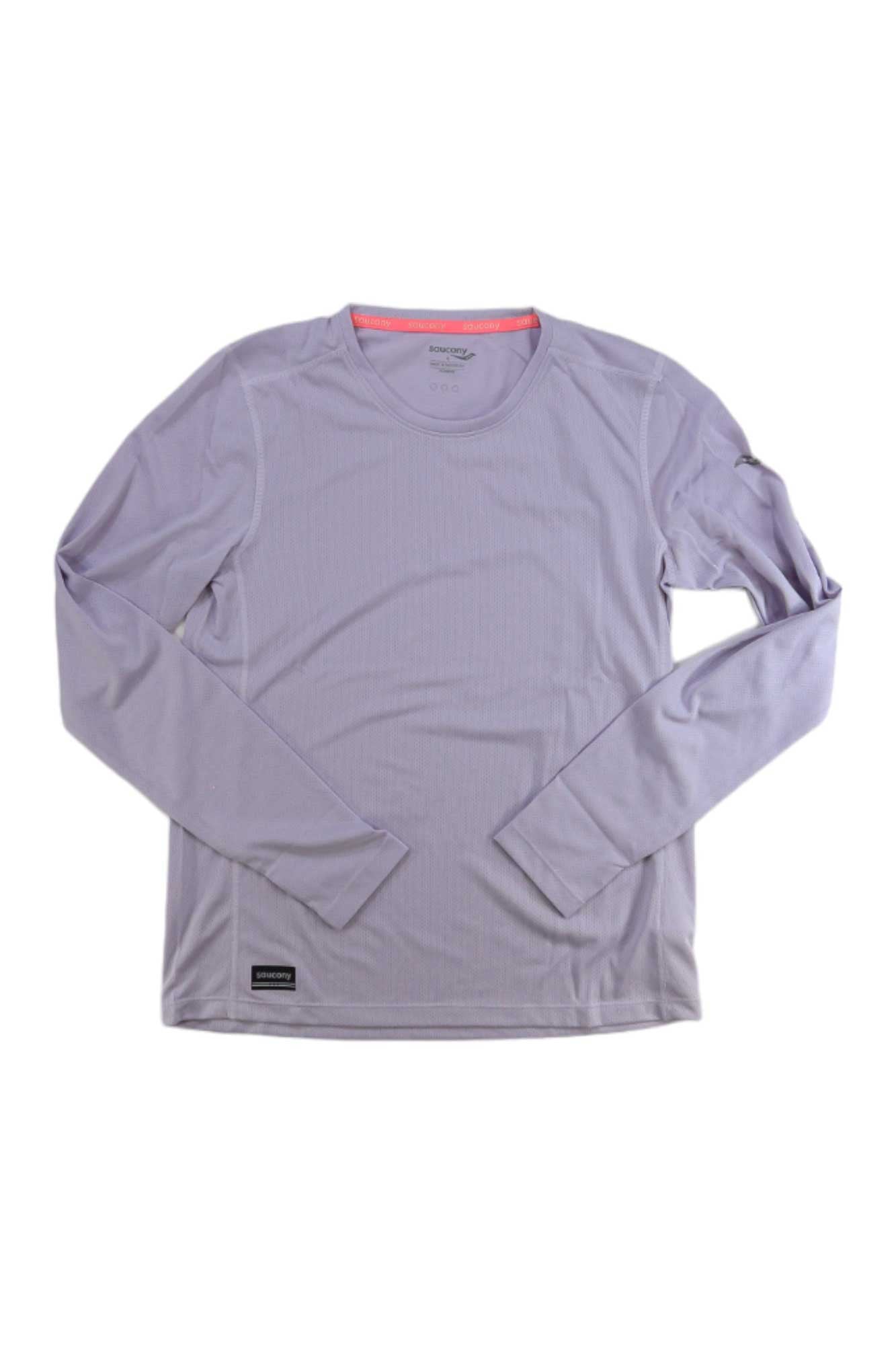 The Saucony Women's Stopwatch LS Top is a light purple long sleeve running shirt with a crew neckline, made from recycled polyester and breathable mesh panels. Laid flat on white, it features a small black rectangular tag near the bottom hem.