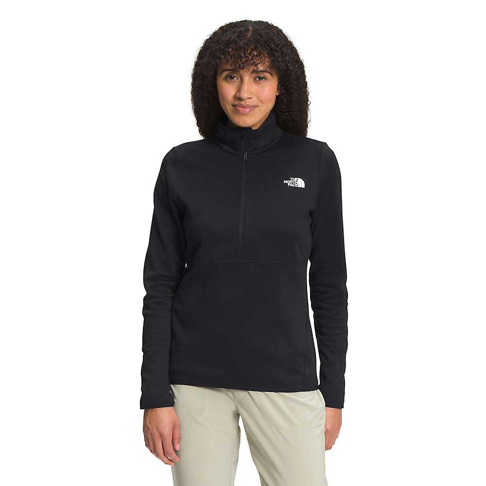 A woman with curly hair smiles while standing against a white background, wearing the black The North Face Womens Canyonlands 1/4 Zip Top and light-colored pants.