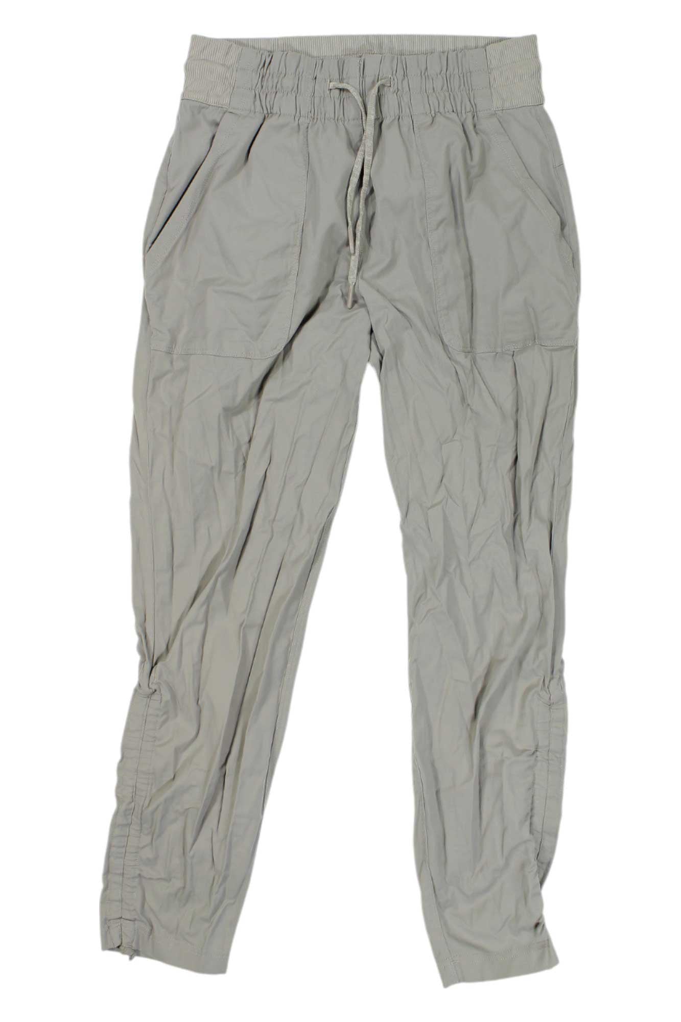The Womens Aphrodite Motion Pants 2.0 are light gray, lightweight hiking pants for women featuring an elastic waistband, drawstring, side pockets, and breathable fabric with a relaxed fit ideal for outdoor activities.