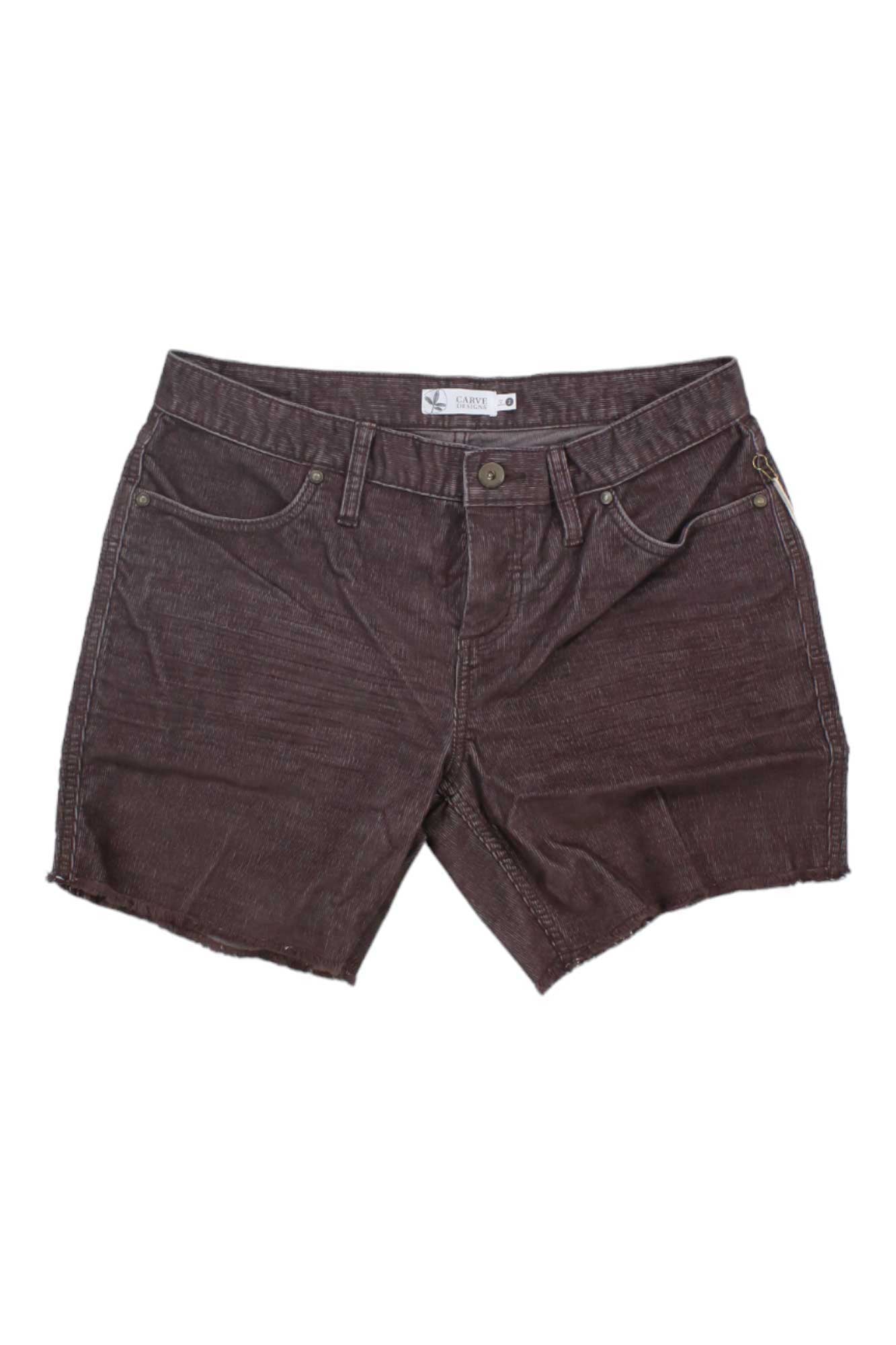 A pair of Carve Designs Womens Oahu 6 Inch Shorts in brown, made from organic cotton with button and zip closure, front and back pockets, and raw hems, is laid flat on a white background.