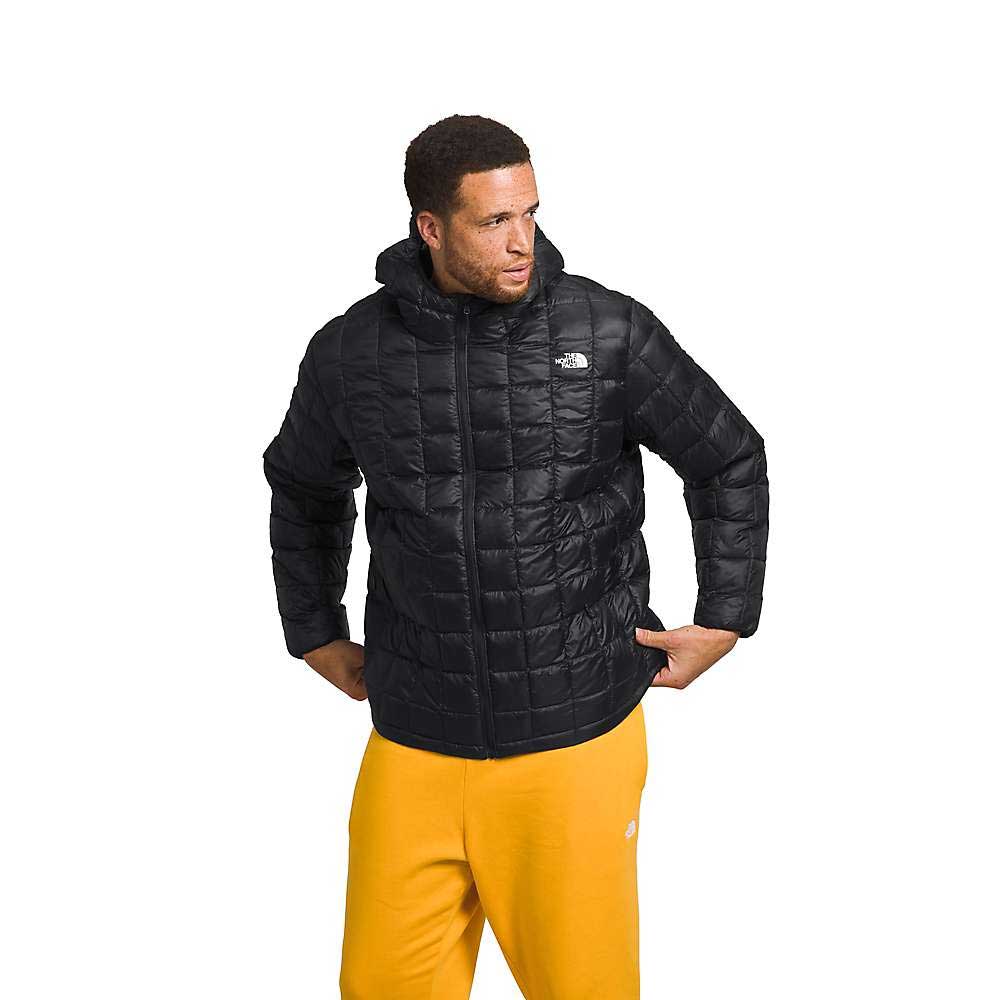 A man in a black The North Face Men's Big Thermoball Eco 2.0 Hoodie and bright yellow sweatpants stands with his hands on his hips against a white background.